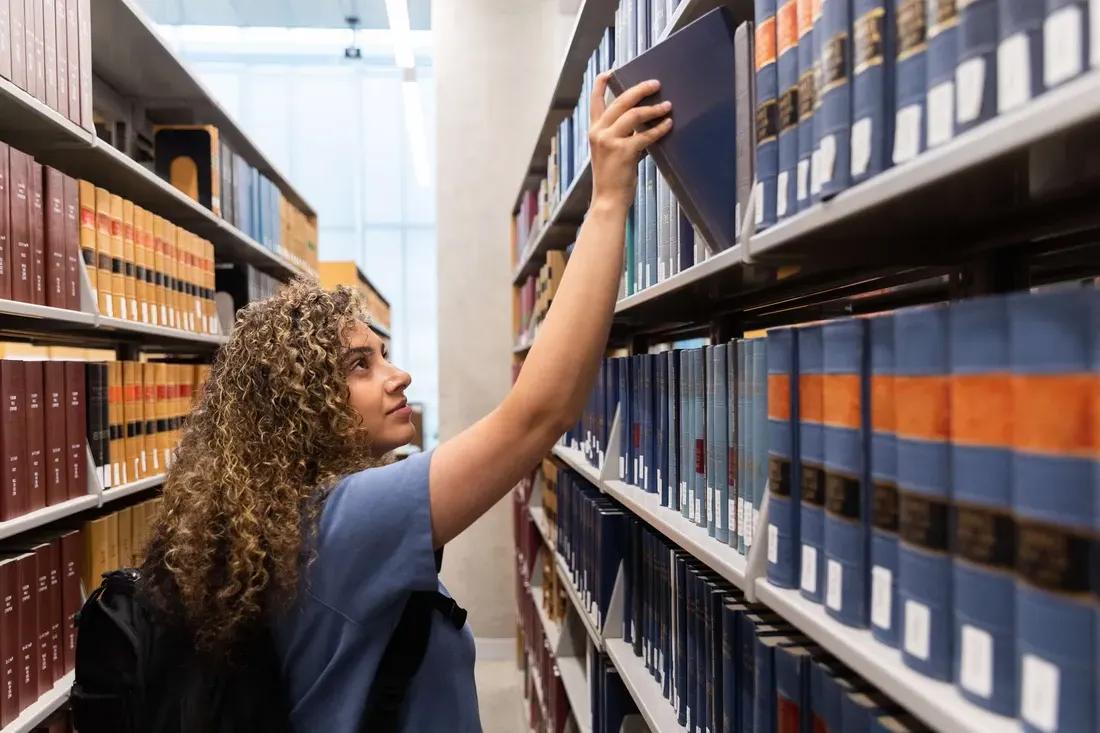 A student taking a book off the shelf at the library.